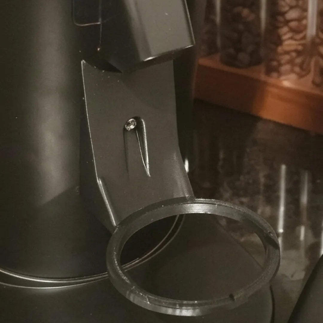 Close-up of a black kitchen appliance with a metal ring on a dark surface.