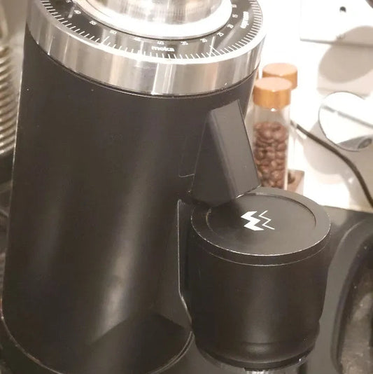 Black coffee grinder with a brand logo on a blurred kitchen background