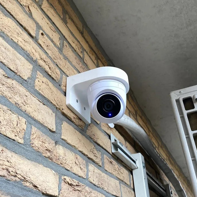 White security camera mounted on a brick wall next to an air conditioning unit.