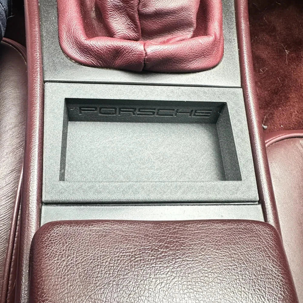 Car interior with a Porsche logo on a gray panel.
